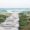 Wooden boardwalk between grass and sand hills leading to blue ocean