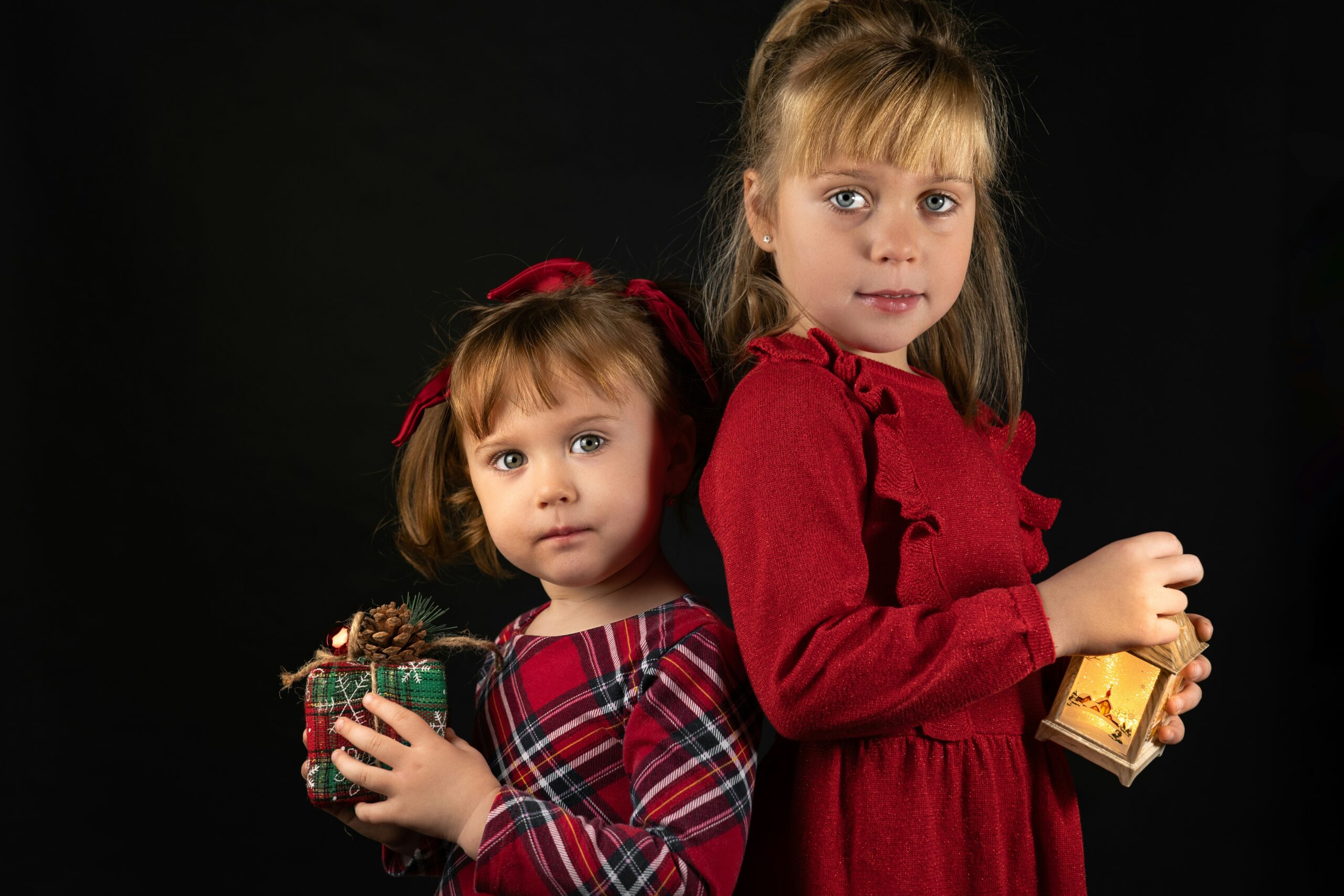 lukas-parnican-sxscElnGXb4-unsplash - Bridging Divorce Solutions Two young girls with serious facial expressions standing back to back wearing Holiday-themed dresses and holding small packages in their hands