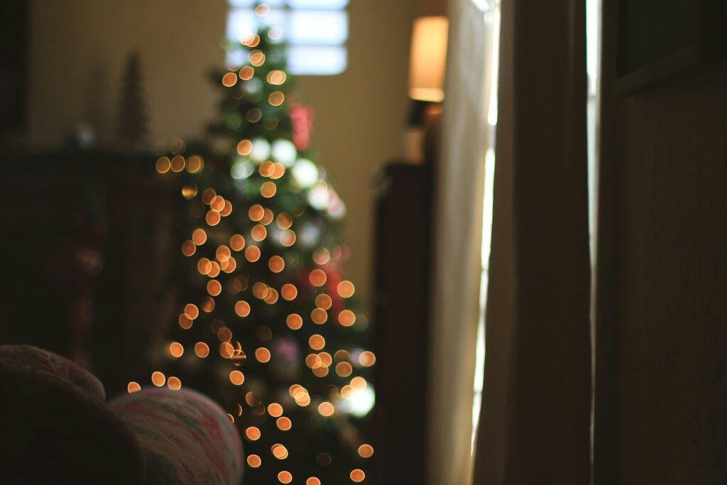 Blurred Christmas tree in back of living room under a window with arm of couch in focus