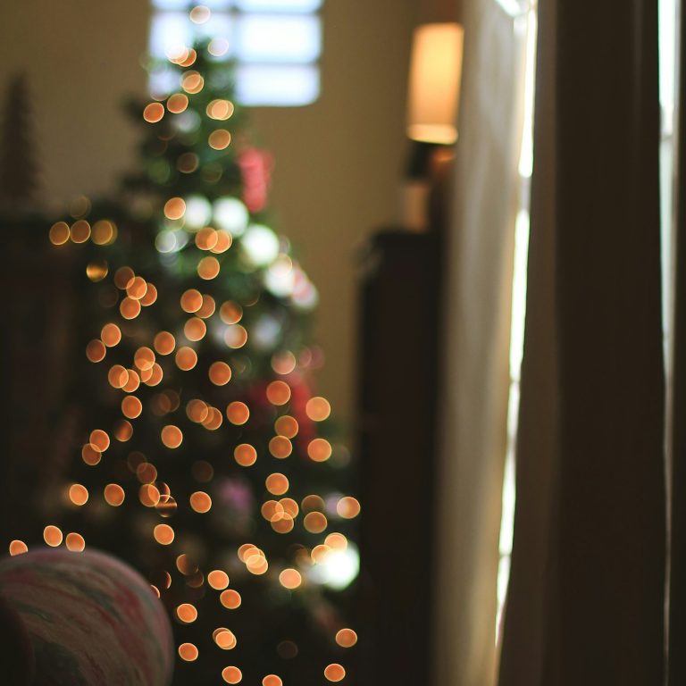 Blurred Christmas tree in back of living room under a window with arm of couch in focus